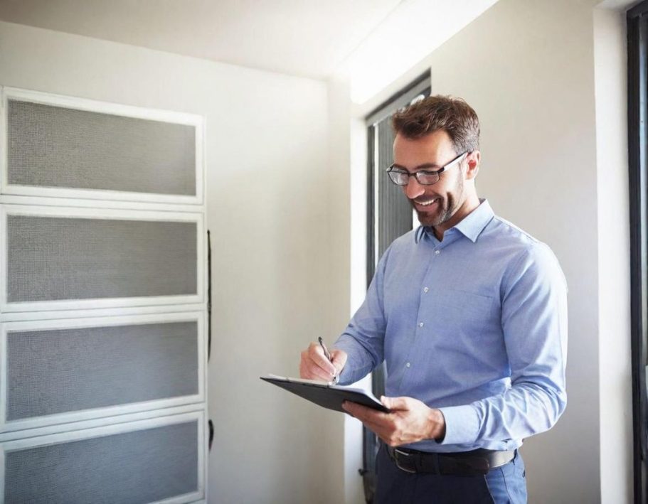 Ein Mann in einem blauen Hemd schreibt Notizen in einem Tablet in einem hellen Raum.