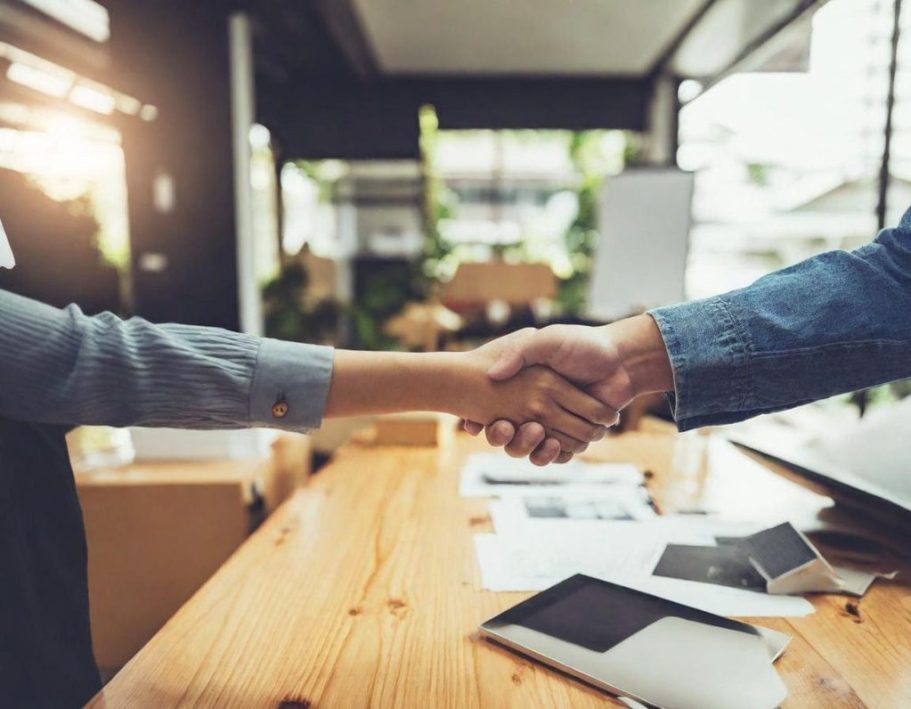 Individueller Vertragsabschluss Zwei Personen schütteln sich die Hände über einem Tisch in einem modernen Büro.