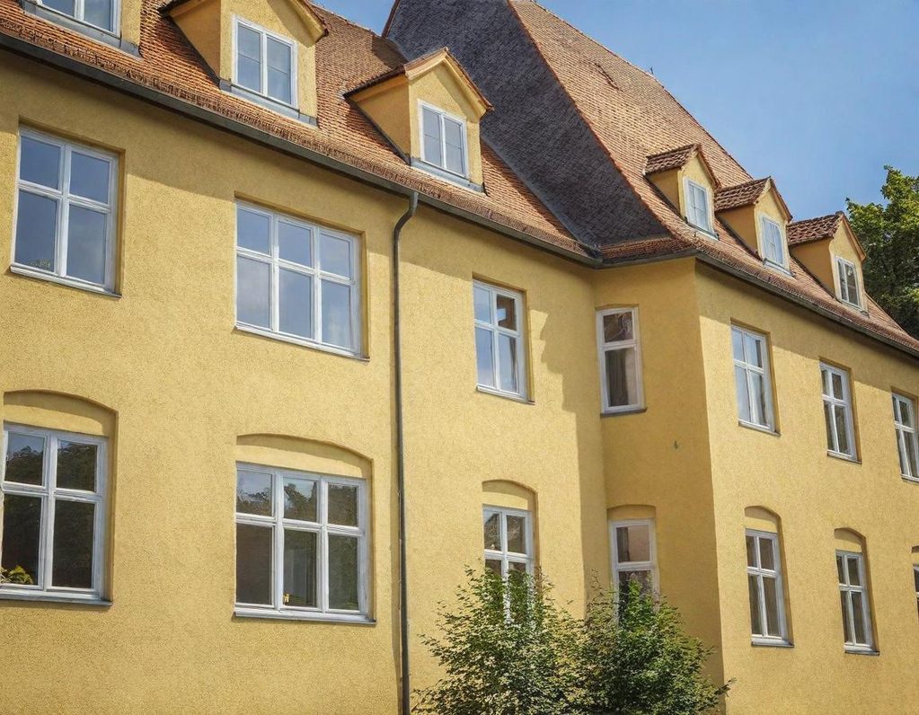 Gelbes Gebäude mit vielen Fenstern und einem steilen Dach, umgeben von Bäumen.